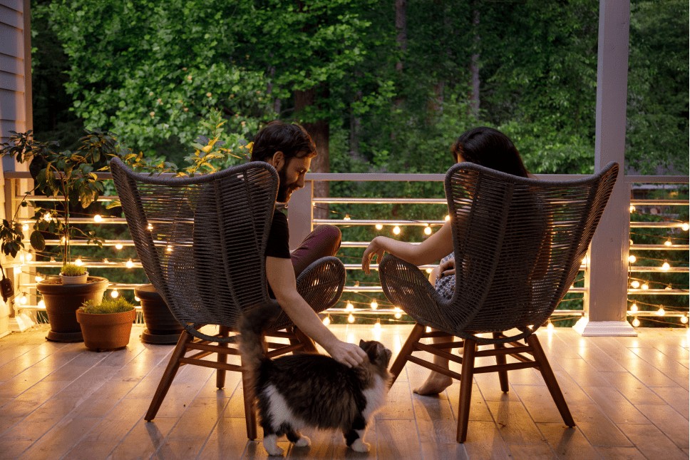 A husband and wife sitting on their back patio surrounded by string lights that make the area cozy
