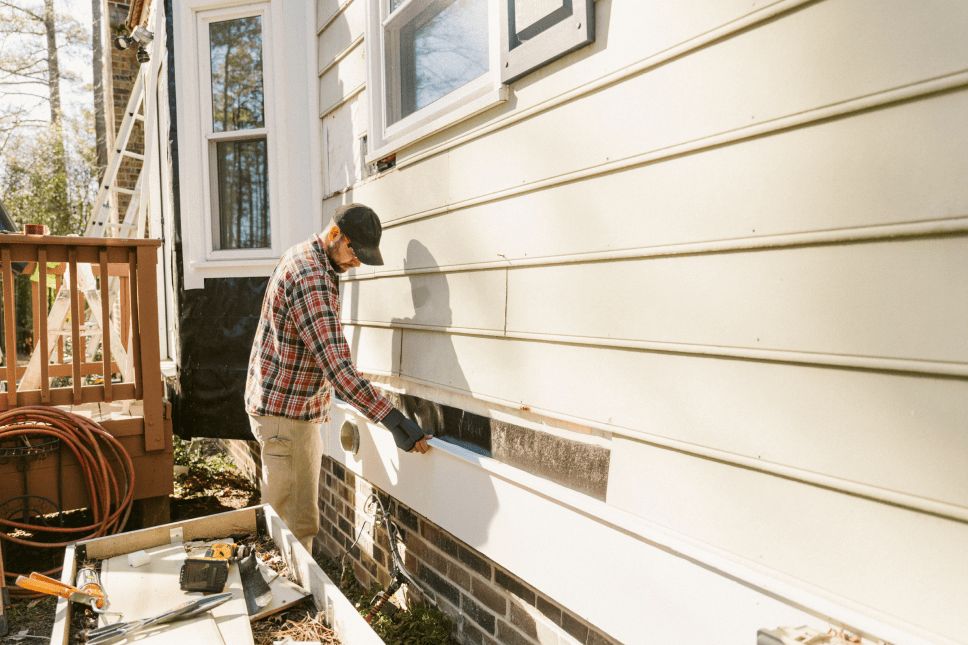 Construction worker repairing house siding on a colonial-style home.