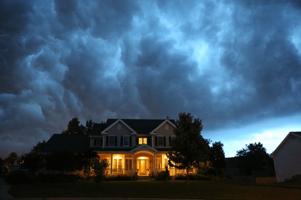 Front view of a home with front porch lights on with a cloudy sky above it.