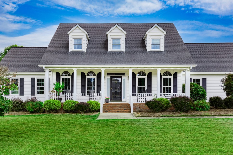 A beautiful white siding home with a large front porch and black shutter accents that has a well-kep